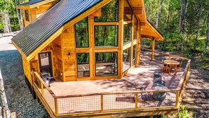 A wooden cabin with a large deck, a fire pit, and a dining area.