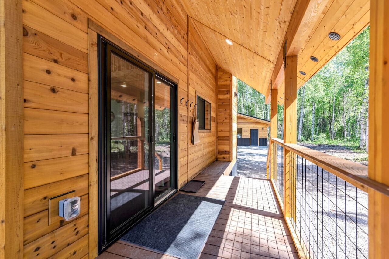 A wooden cabin with a covered porch, large windows, and a door leading to an outdoor area.