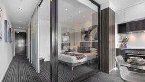 Een moderne hotelkamer met een glazen scheidingswand, een bed, een bureau en een kitchenette.