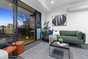 A modern living room with a green sofa, a black coffee table, and a glass door leading to an outdoor area.