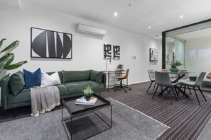 A modern living room with a green sofa, a coffee table, and a dining area with a glass table and chairs. - Luxurious Fitzroy Street Getaway (St Kilda)