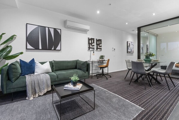 A modern living room with a green sofa, a coffee table, and a dining area with a glass table and chairs.