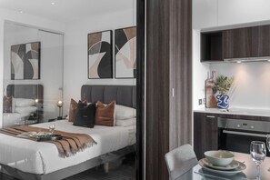 A modern hotel room with a bed, bedside table, and a dining area with a table and chairs.