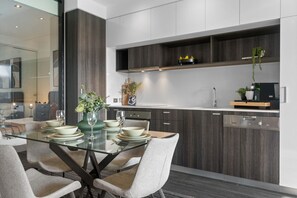 A modern kitchen with dark wood cabinets, a glass dining table, and a built-in oven.