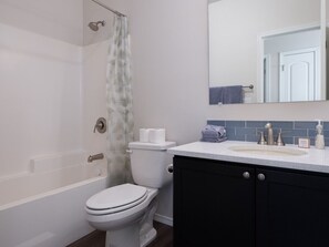 A modern bathroom with a bathtub, toilet, and a vanity with a sink and mirror. - Modern Home with Panoramic Teton Views (Tetonia)