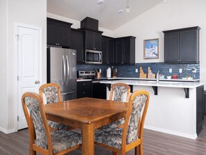 A modern kitchen with dark cabinets, a stainless steel refrigerator, a microwave, and a tiled backsplash. - Modern Home with Panoramic Teton Views (Tetonia)