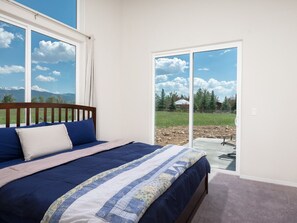 A bedroom with a large bed, a wooden headboard, and a view through a sliding glass door to an outdoor patio. - Modern Home with Panoramic Teton Views (Tetonia)