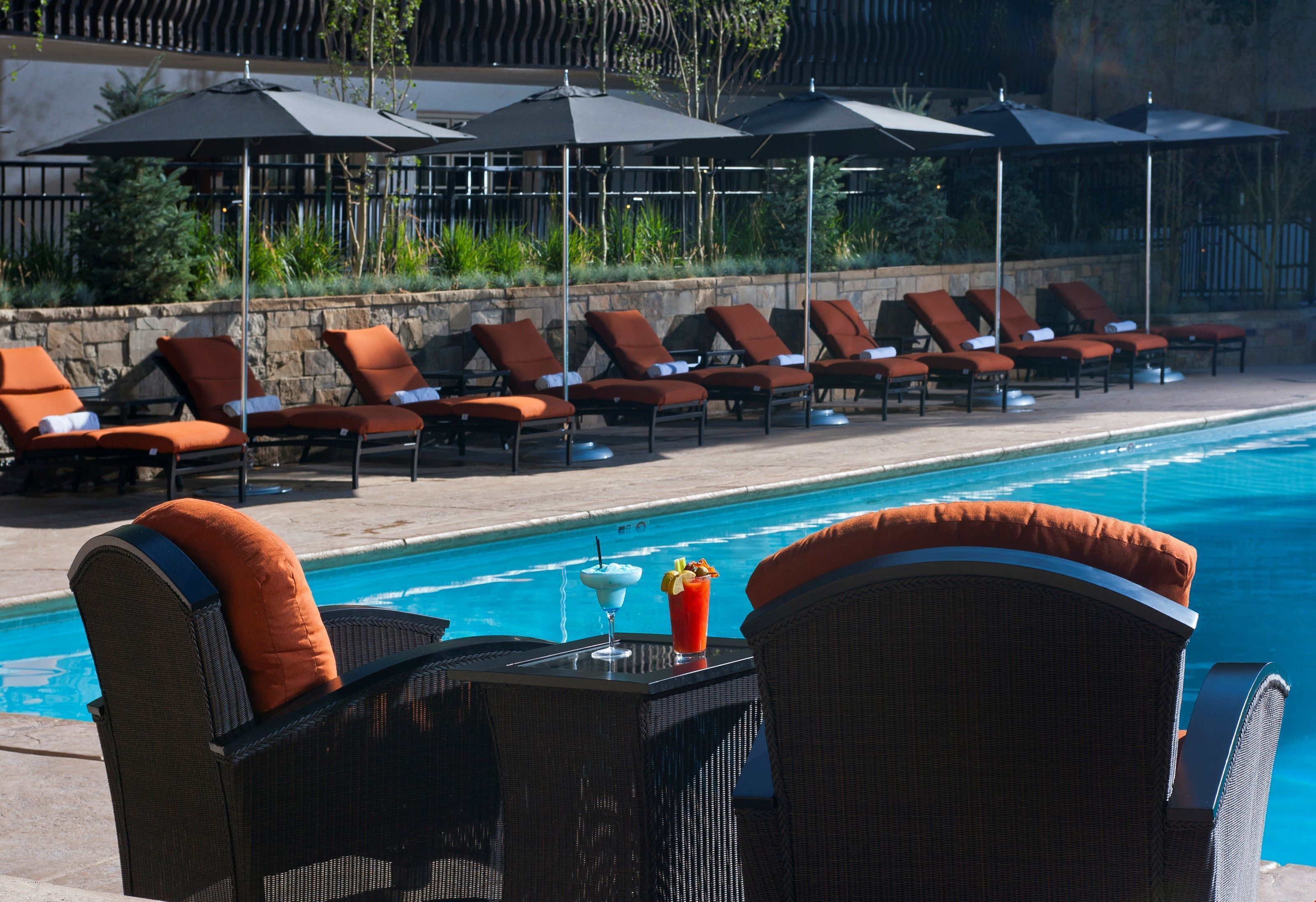 Un espace aménagé au bord de la piscine, avec des chaises longues et des parasols, une table avec des boissons et une vue dégagée sur la piscine.