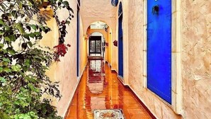 A narrow alleyway with a tiled floor, a blue door on the right, and a white door at the end. - Hôtel Villamar (Hammamet)