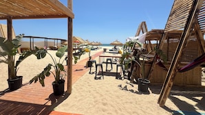 A beachside area with wooden structures, tables, chairs, and potted plants. - Hôtel Villamar (Hammamet)