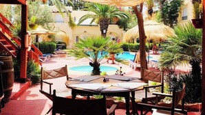 An outdoor patio with a pool, wooden furniture, and tropical plants. - Hôtel Villamar (Hammamet)