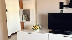 A modern hotel room with a flat-screen TV, a white dresser, and a small shelf with a vase of sunflowers. - SE123 - Marzocca, three-room apartment 300 meters from the sea (Marzocca)