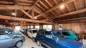 A car showroom with multiple vehicles, wooden ceiling beams, and a sign indicating a society.