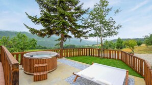 A wooden deck with a hot tub, a lounge chair, and a view of a mountainous landscape.