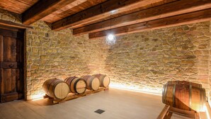 A stone-walled room with wooden beams, a wooden door, and several wooden barrels.