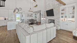 A spacious living area with a large sectional sofa, a fireplace, and a kitchen with white cabinetry.