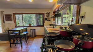 Una cocina con estufa, ollas, un lavamanos y una zona de comedor con taburetes.