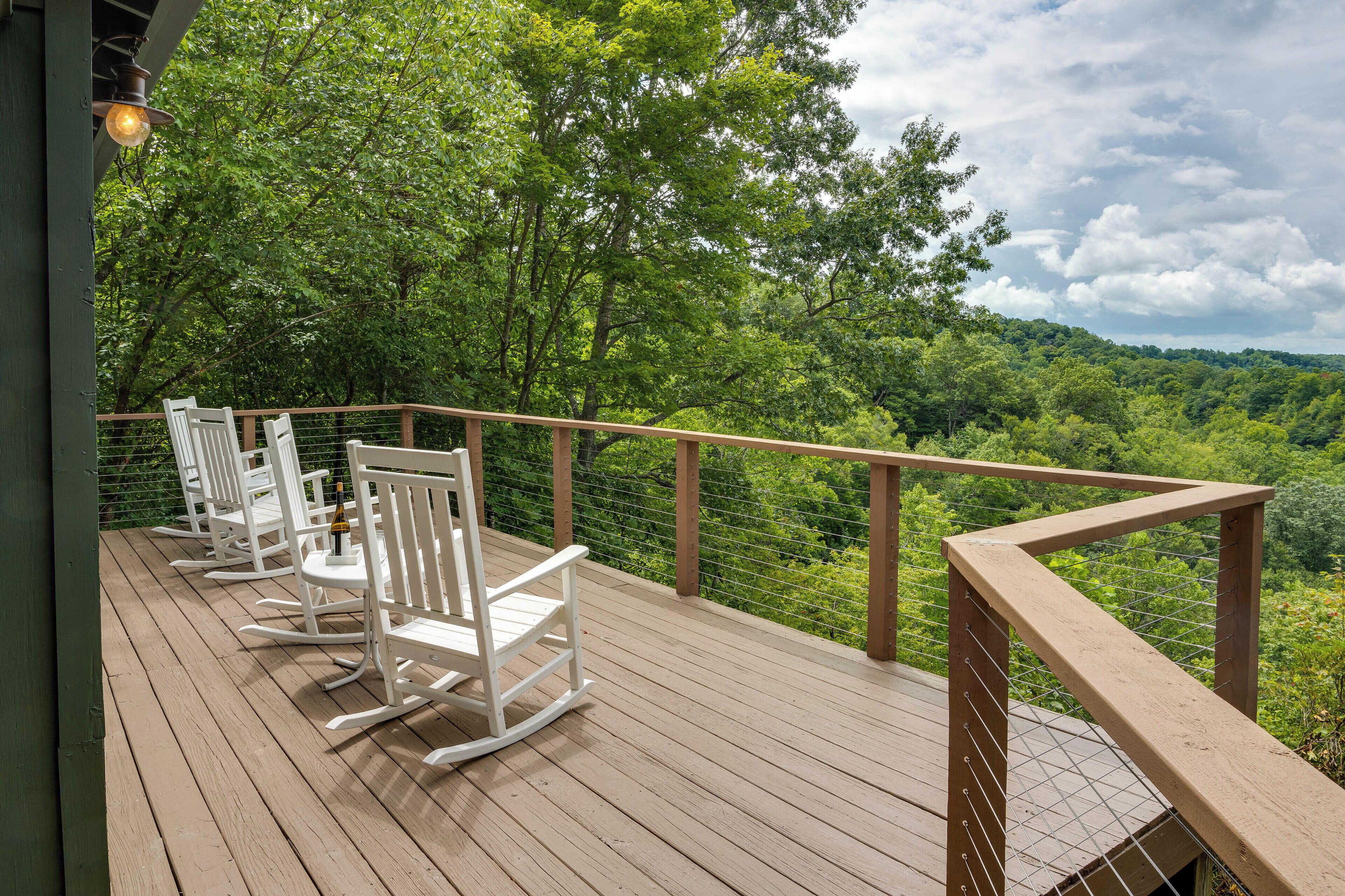 A wooden deck with white rocking chairs and a view of a lush green forest.
