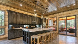 Una cocina amplia con armarios de madera oscura, una isla grande con taburetes y vistas al exterior a través de puertas correderas de vidrio.