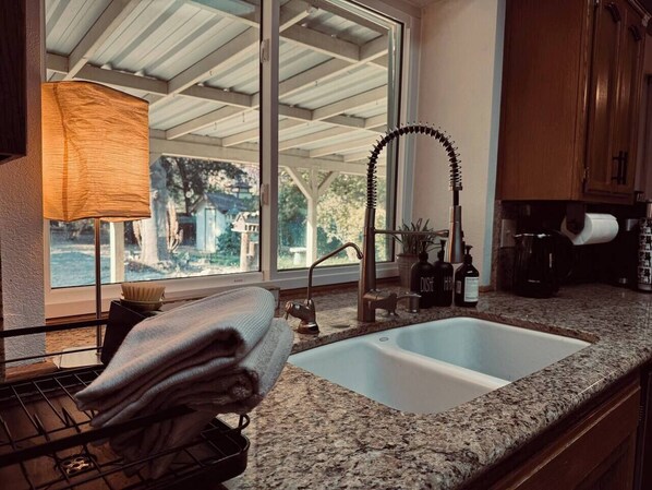 Una cocina con encimera de granito, un lavamanos doble y una ventana con vista a árboles.