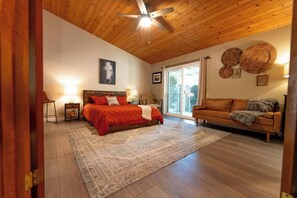 Un dormitorio con techo de madera, una cama con ropa de cama roja, un sofá y un tapete grande.