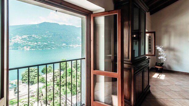 A room with a large window overlooking a scenic view of a lake and mountains. - Lake Frame - MyHomeinComo (Blevio)