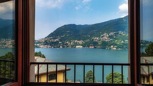 A view through a window of a mountainous landscape with a body of water, buildings, and a clear sky. - Lake Frame - MyHomeinComo (Blevio)