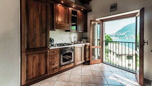 A kitchen with wooden cabinets, a stove, and an oven. There is a window with a view of a mountain and a balcony. - Lake Frame - MyHomeinComo (Blevio)