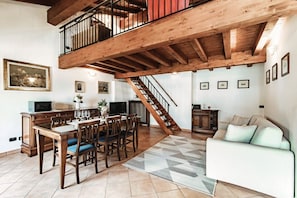 A dining area with a wooden table and chairs, a staircase, and a white sofa. - Lake Frame - MyHomeinComo (Blevio)