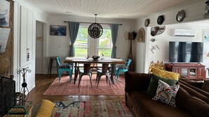 A dining area with a wooden table and chairs, a hanging light fixture, and a view of the outdoors through large windows. - Lake house 35 from Auburn and Ft. Benning (Salem)