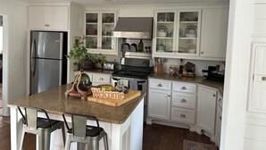 A kitchen with white cabinetry, a stainless steel refrigerator, a granite countertop, and a 'Welcome' sign. - Lake house 35 from Auburn and Ft. Benning (Salem)