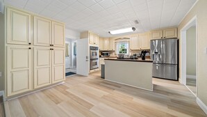 A spacious kitchen with light wood flooring, white cabinets, and stainless steel appliances.