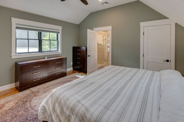 A bedroom with a large bed, a dresser, a window, and a door leading to a bathroom.
