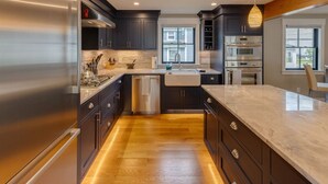 A modern kitchen with dark cabinetry, stainless steel appliances, and a marble countertop. - Luxury House in Lincoln (Lincoln)