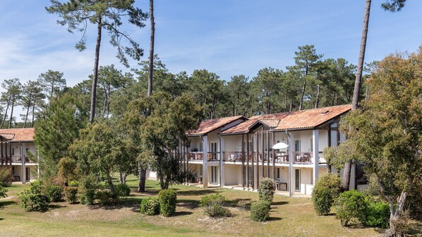 A row of two-story cabins with balconies, surrounded by pine trees and a well-maintained lawn.