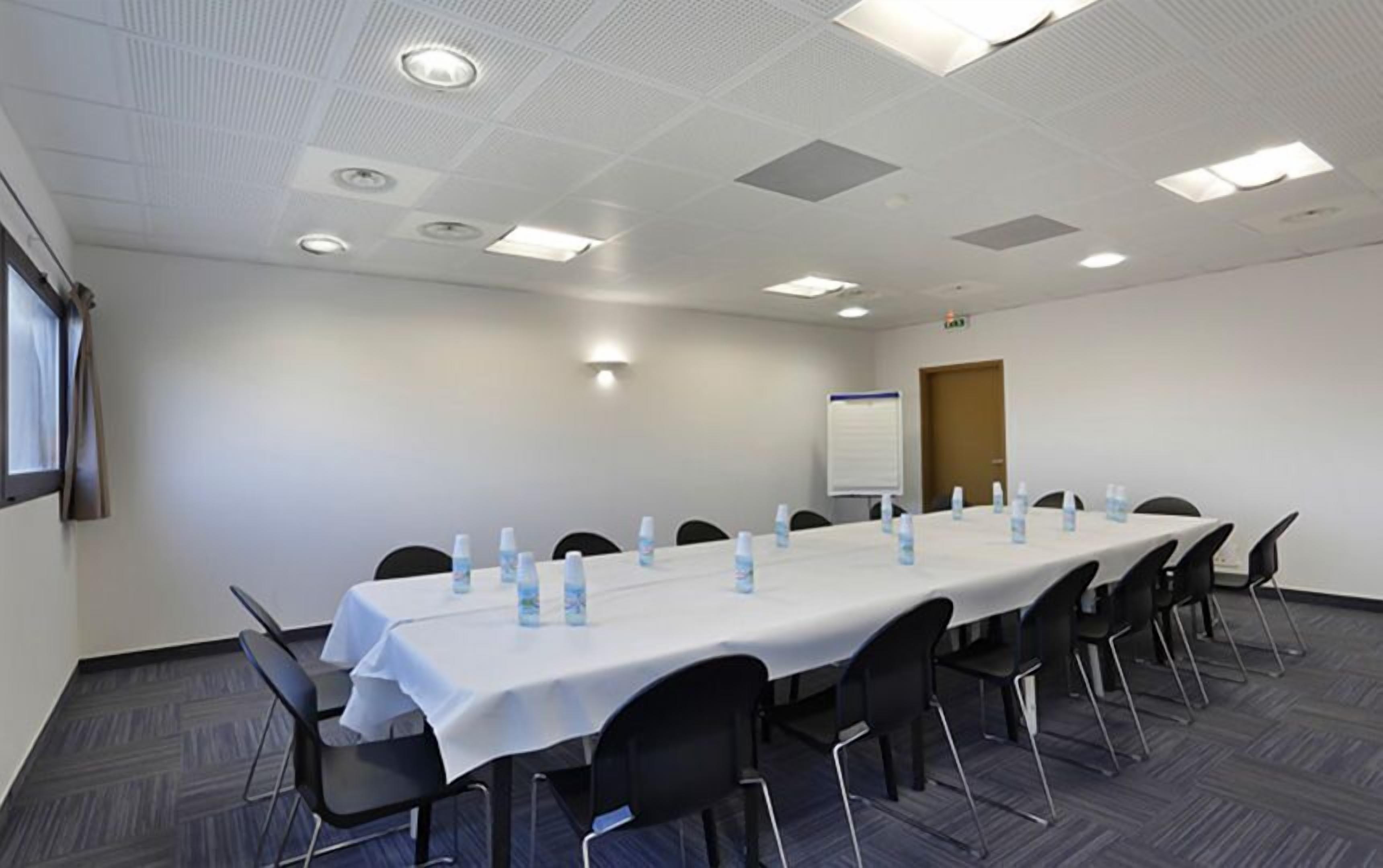 Een vergaderruimte met een lange tafel, stoelen, waterflesjes en een whiteboard.
