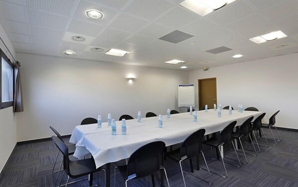 Un salón de conferencias con una larga mesa, sillas, botellas de agua y una pizarra.