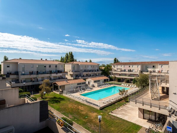 A residential building with a swimming pool, balconies, and a clear sky.