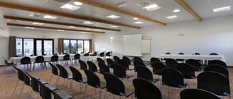 Un salón de conferencias con varias mesas y sillas, ventanas amplias y una pizarra.