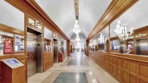 A long corridor with wooden paneling, marble flooring, and a central chandelier.