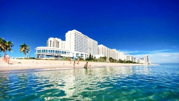 A beachfront hotel with multiple high-rise buildings, clear blue water, and a sandy beach.