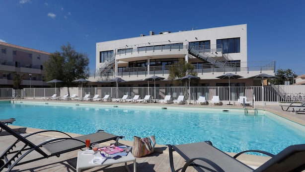 A pool area with lounge chairs and umbrellas, a modern building with a staircase, and a clear blue sky.
