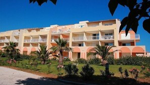 Un hotel de varios pisos con balcones, rodeado de palmeras y un jardín cuidado.