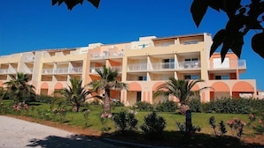 A multi-story hotel with balconies, surrounded by palm trees and a well-maintained garden.