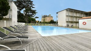 A swimming pool with lounge chairs, a wooden deck, and a building in the background.