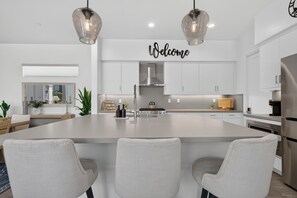 A modern kitchen with a large island, stainless steel appliances, and a 'Welcome' sign above the counter.