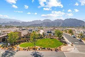 A residential area with houses, a green lawn, and mountains in the background. - El Encanto: EV Charger, Pool, Spa & BBQ (La Quinta)
