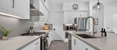 Una cocina moderna con armarios blancos, estufa de acero inoxidable y horno empotrado.