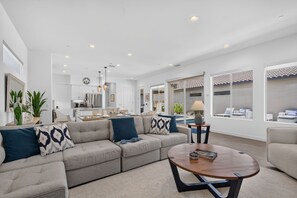 A modern living room with a sectional sofa, a round coffee table, and a dining area in the background.