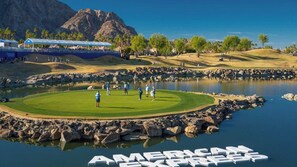 A golf course with a water body, a mountain in the background, and a large sign reading 'AMERICAN EXPRESS'. - El Encanto: EV Charger, Pool, Spa & BBQ (La Quinta)